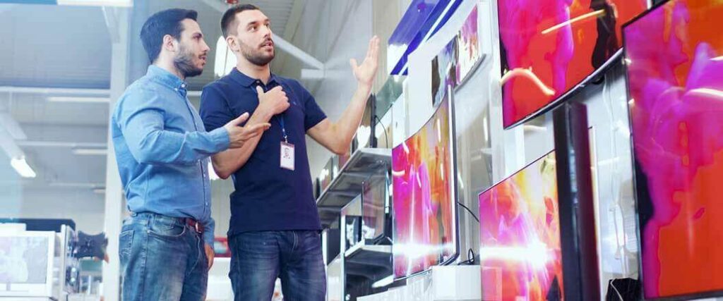 A customer and a sales associate looking at different tv's in a store