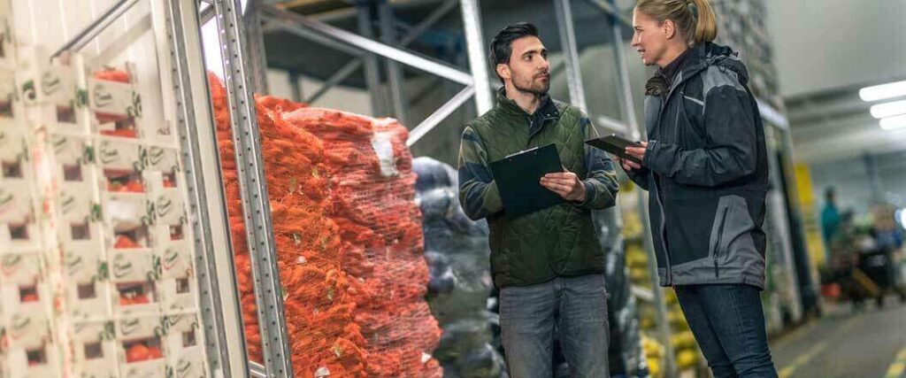 CBP inspectors in a warehouse standing next to palletized fruits and vegetables.