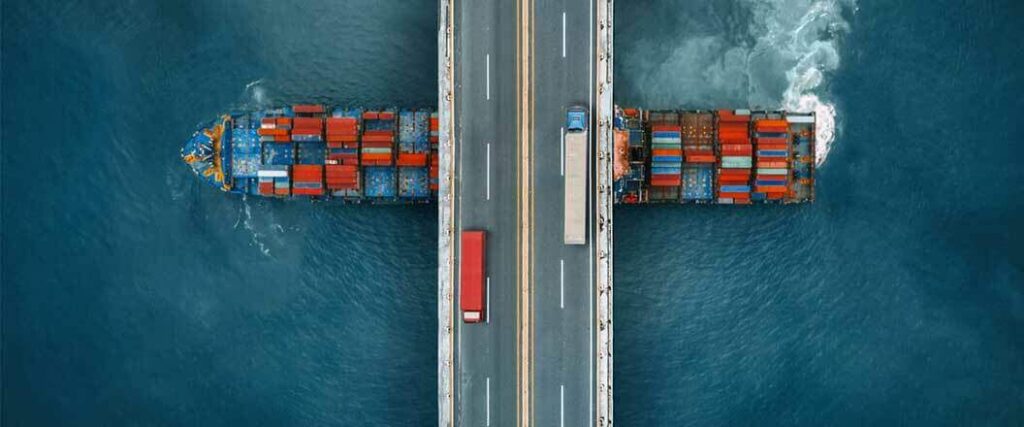 An overhead view of semi trucks crossing a bridge with a cargo vessel passing underneath the bridge.