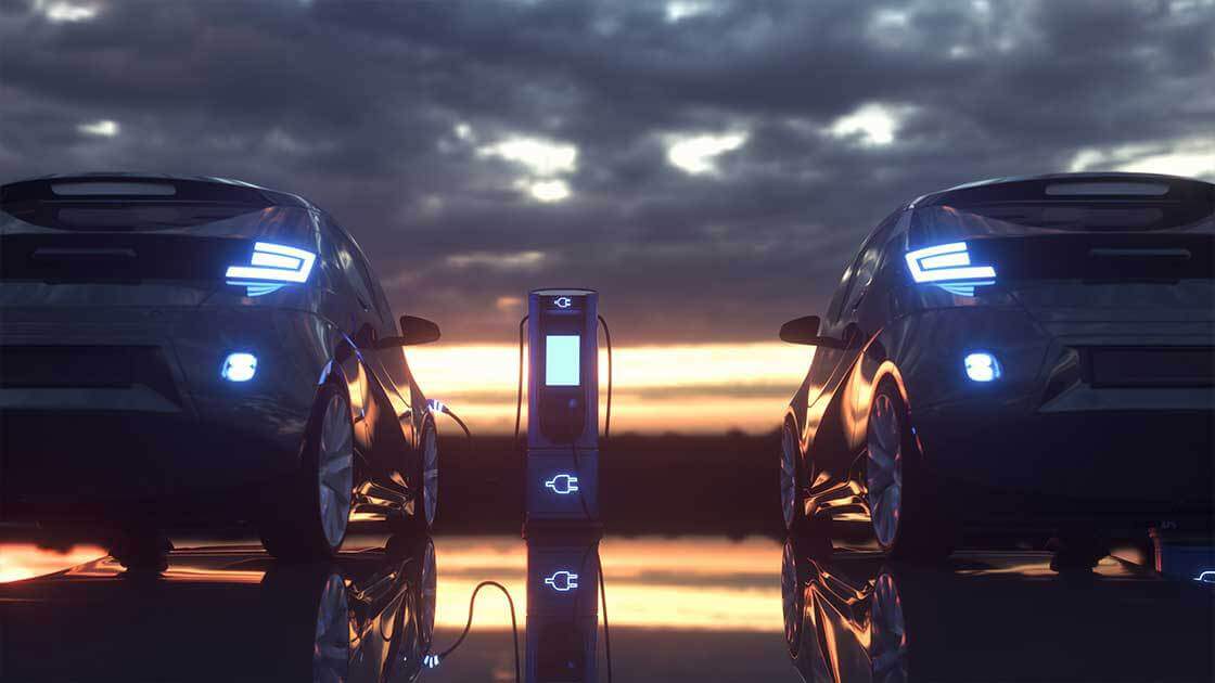 Two electric vehicles at a charging station at sunset