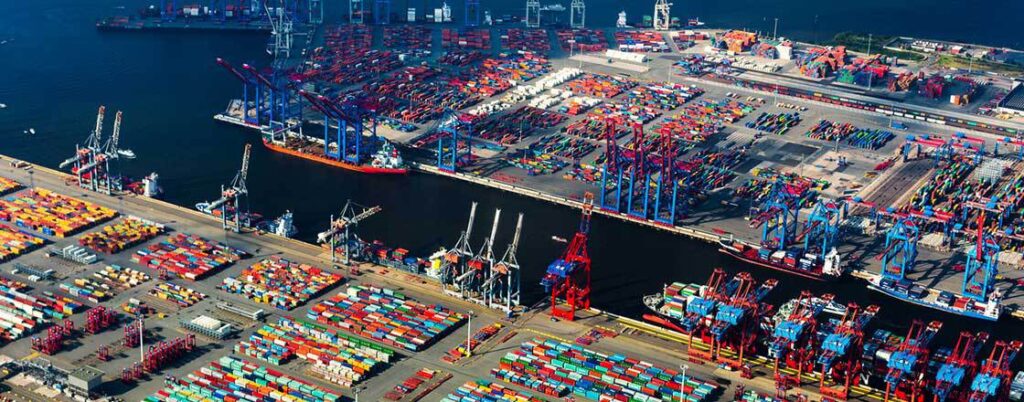 Another aerial view of a port with cargo containers, docked cargo ships and cranes