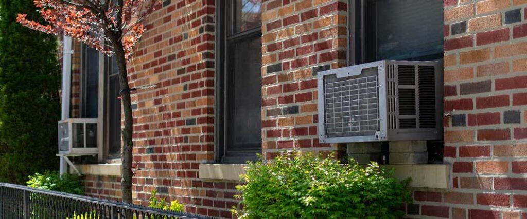A window ac unit mounted in the window of a brick house.