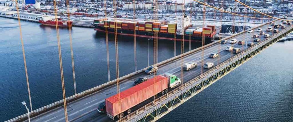 A truck transporting a container over a bridge with a port on the other side.