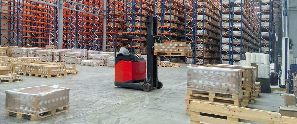 A solitary red forklift loaded with pallets sitting at port.