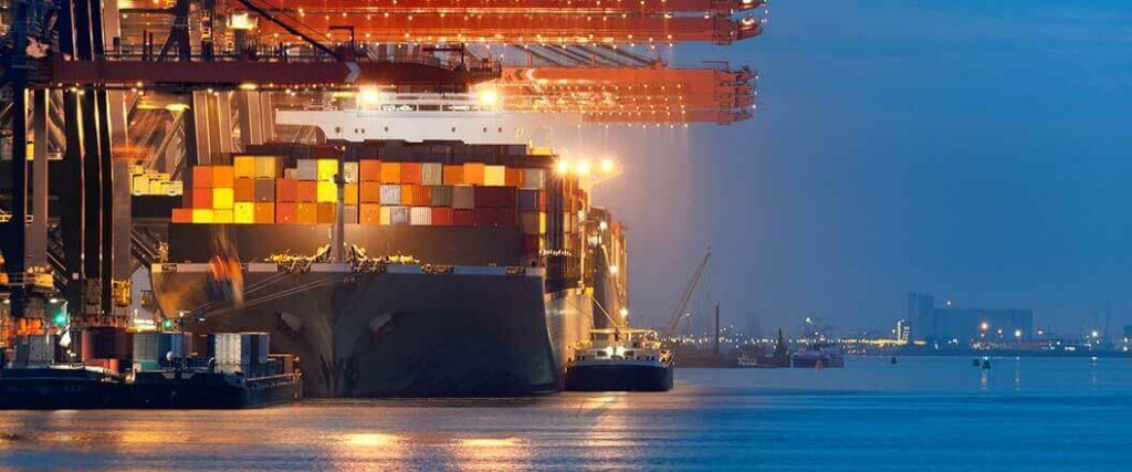 A container ship is docked at a port terminal at night preparing to be unloaded. 