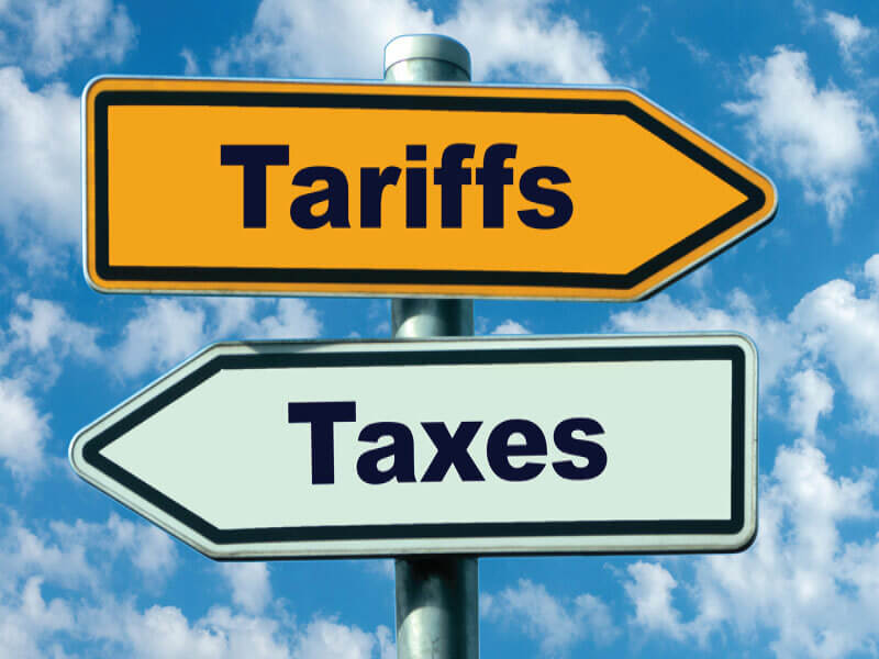 A road sign with two arrows: the top arrow is yellow and labeled "tariffs" pointing to the right while the bottom arrow is painted pale green and is labeled "taxes, pointing to the left. This supports the article title "tariff vs tax"